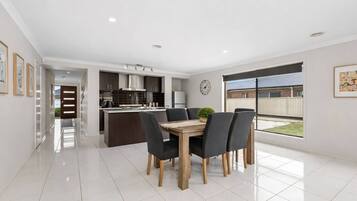 A modern kitchen with dark cabinetry, a central island, and a dining area with a wooden table and chairs.