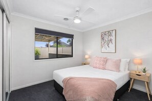 A bedroom with a bed, bedside tables, a ceiling fan, a window with a view, and a wall-mounted artwork.