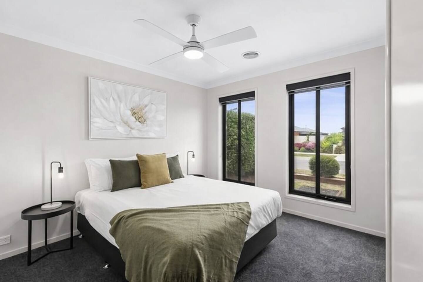 Une chambre à coucher comprenant un lit, un ventilateur de plafond, une table de chevet, une fenêtre et une œuvre d’art accrochée au mur.