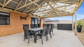 A covered patio with a table and chairs, a brick wall, and a metal roof structure.