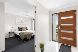 A modern bedroom with a bed, bedside tables, a ceiling fan, and a large window. - Chifley Place Modern Comfort near Delacombe Town (Delacombe)