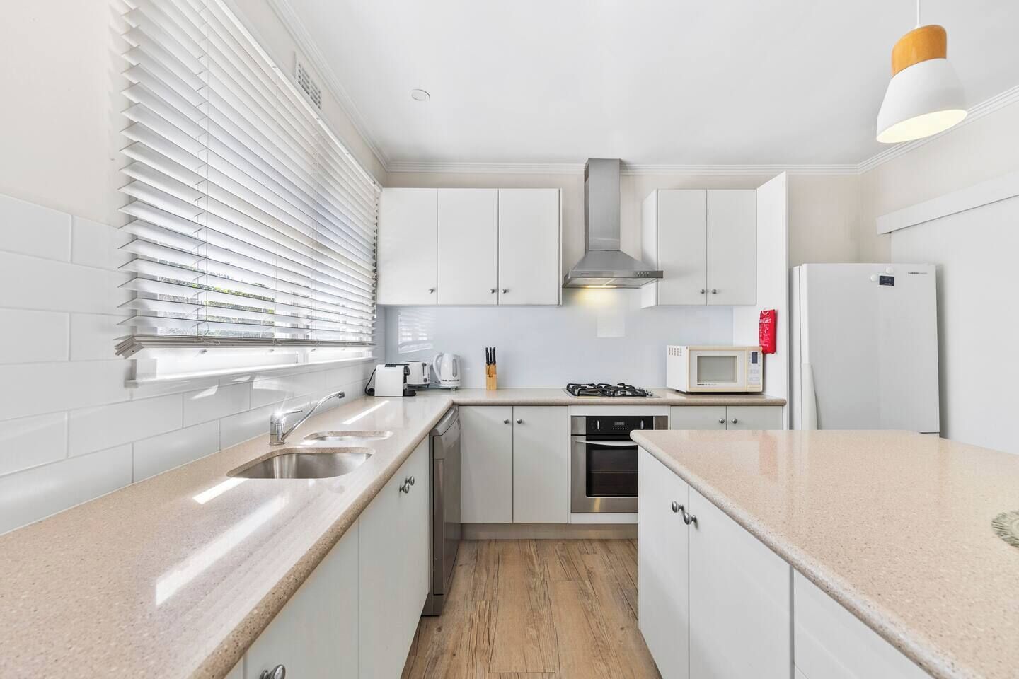 A modern kitchen with white cabinets, stainless steel appliances, and a wooden floor.