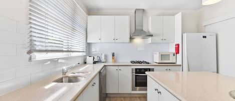 A modern kitchen with white cabinets, stainless steel appliances, and a wooden floor.