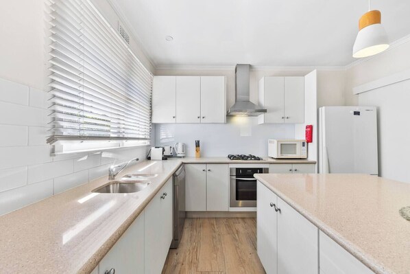 A modern kitchen with white cabinets, stainless steel appliances, and a wooden floor.