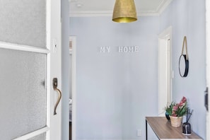 Ein Flur mit einer Tür, einem an der Wand befestigten Schild mit der Aufschrift 'MY HOME', einer Pendelleuchte und einem kleinen Tisch mit Pflanze und Kerzenständer.