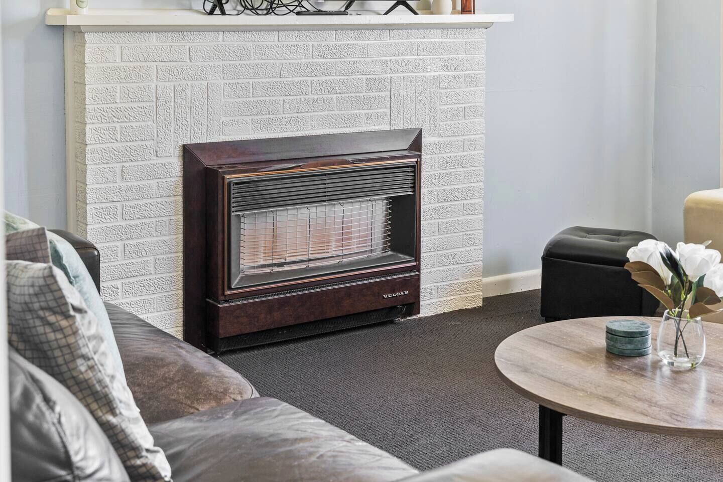 A room with a fireplace, a sofa, a coffee table, and a vase with flowers.