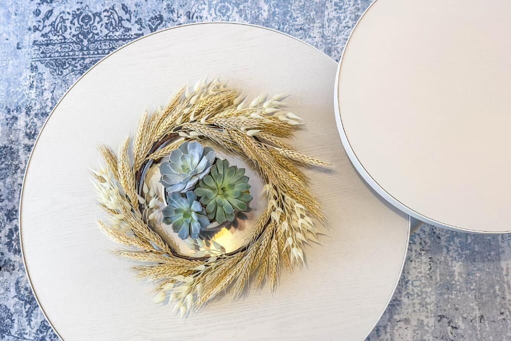 A round table with a decorative arrangement of wheat and succulents.