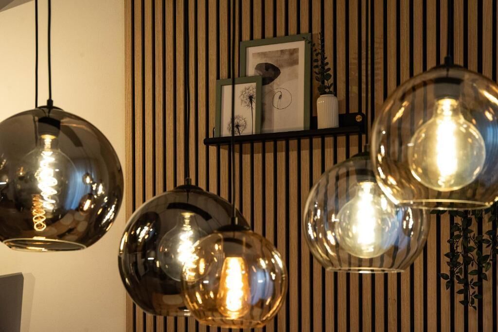 A room with a striped wall, a black shelf with framed pictures, and three spherical pendant lights.