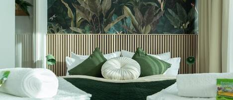 A hotel room with a bed centered between two windows, a large tropical-themed mural on the wall, and a wooden headboard.