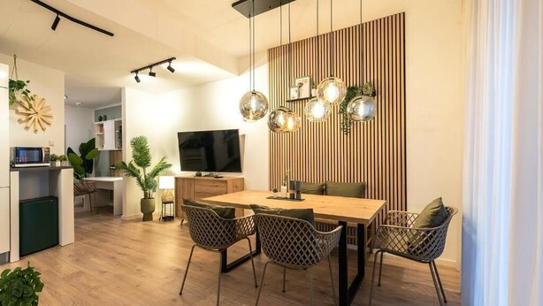 A modern dining area with a wooden table and chairs, a television, and a decorative wall panel.