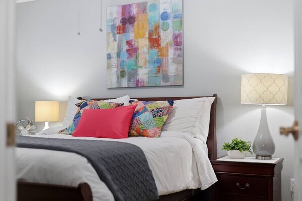 A neatly made bed with a colorful quilt and pillows, a bedside lamp, a small bedside table with a plant, and a wall art piece. - Waterfront Condo 10 Min from Margaritaville! (Montgomery)