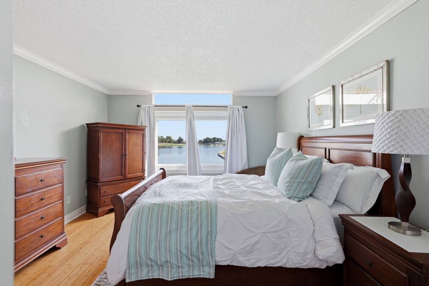 A bedroom with a bed, a dresser, a nightstand, and a view of a lake.
