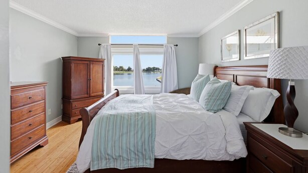 A bedroom with a bed, a dresser, a nightstand, and a view of a lake. - Waterfront Condo 10 Min from Margaritaville! (Montgomery)