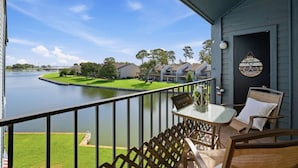 A balcony with a view of a lake, a small table with a sign, and a chair. - Waterfront Condo 10 Min from Margaritaville! (Montgomery)