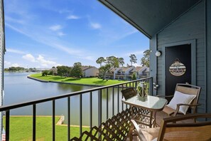 A balcony with a view of a lake, a small table with a sign, and a chair. - Waterfront Condo 10 Min from Margaritaville! (Montgomery)