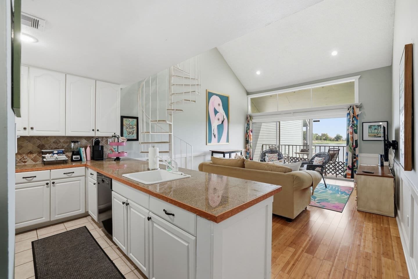 A modern kitchen with white cabinets, a central island, and a dining area with a sofa and chairs.