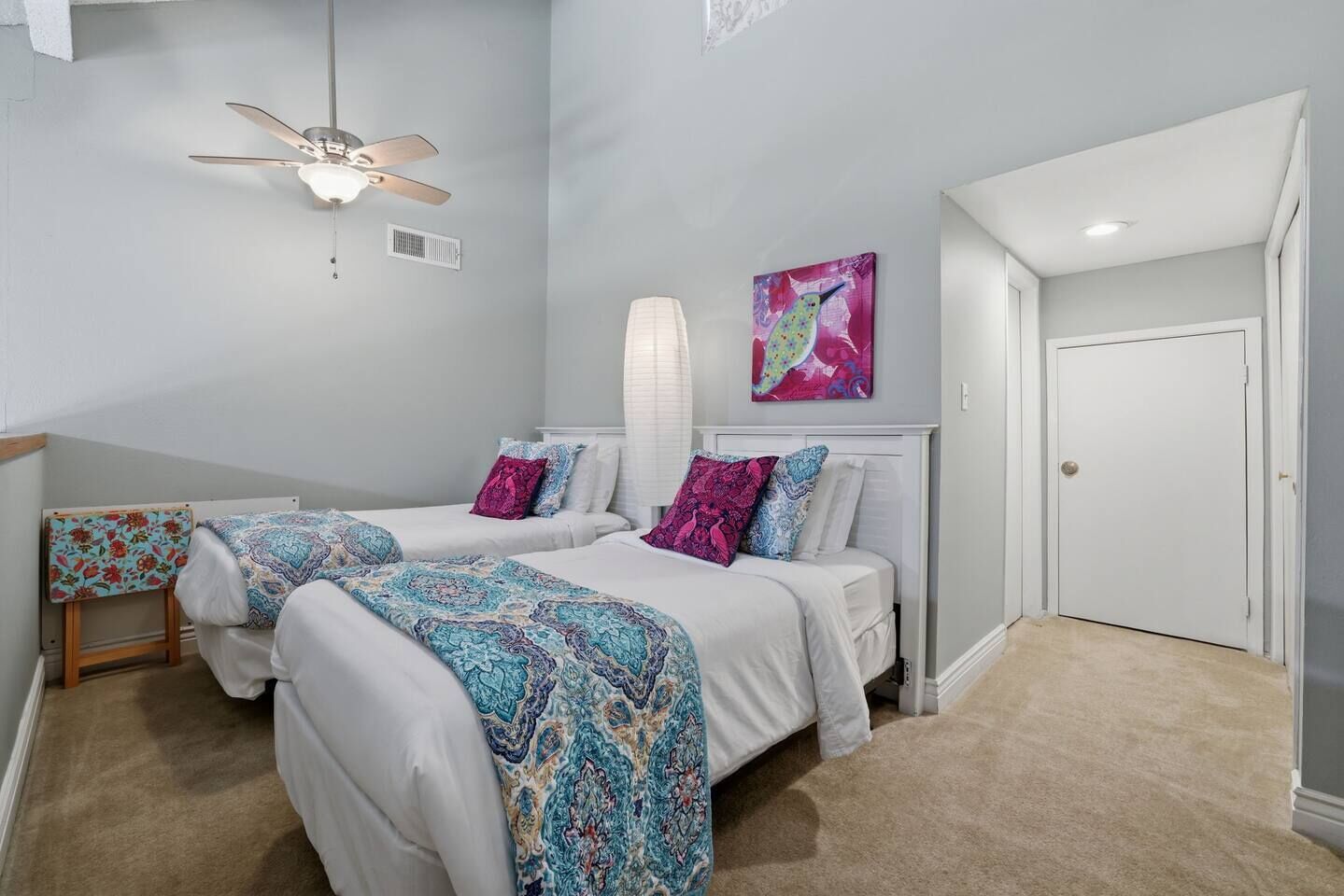 A bedroom with two beds, a ceiling fan, a radiator, and a door.