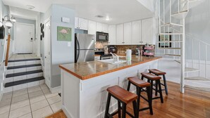 A modern kitchen with a central island, bar stools, and a staircase leading to an upper level. - Waterfront Condo 10 Min from Margaritaville! (Montgomery)