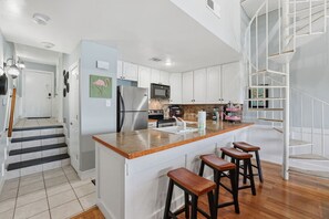 A modern kitchen with a central island, bar stools, and a staircase leading to an upper level. - Waterfront Condo 10 Min from Margaritaville! (Montgomery)