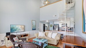 A living room with a sofa, coffee table, and a television. There is a staircase leading to a kitchen area. - Waterfront Condo 10 Min from Margaritaville! (Montgomery)