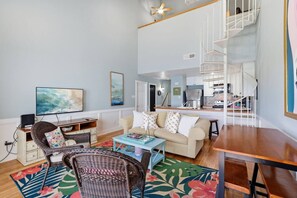 A living room with a sofa, coffee table, and a television. There is a staircase leading to a kitchen area. - Waterfront Condo 10 Min from Margaritaville! (Montgomery)