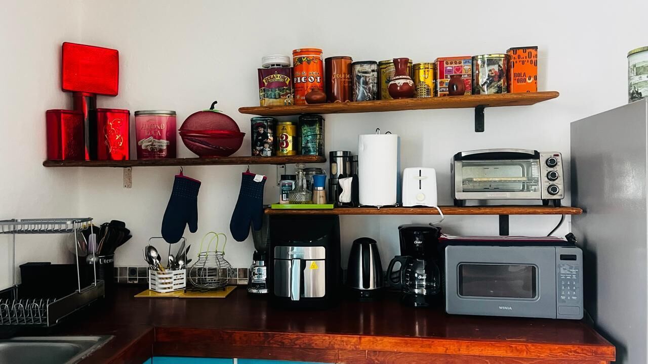 Une cuisine équipée d’un four à micro-ondes, d’un grille-pain, d’une machine à café et de diverses conserves rangées sur des étagères.