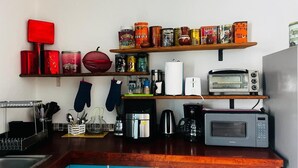 Una cocina con microondas, tostadora, cafetera y diversos alimentos enlatados en los estantes.