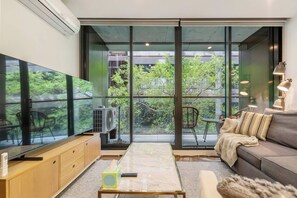 A modern living room with a large flat-screen TV, a sofa, a coffee table, and a dining area with chairs. - Parque Canopy Lakeside Living with Infinity Pool (Melbourne)