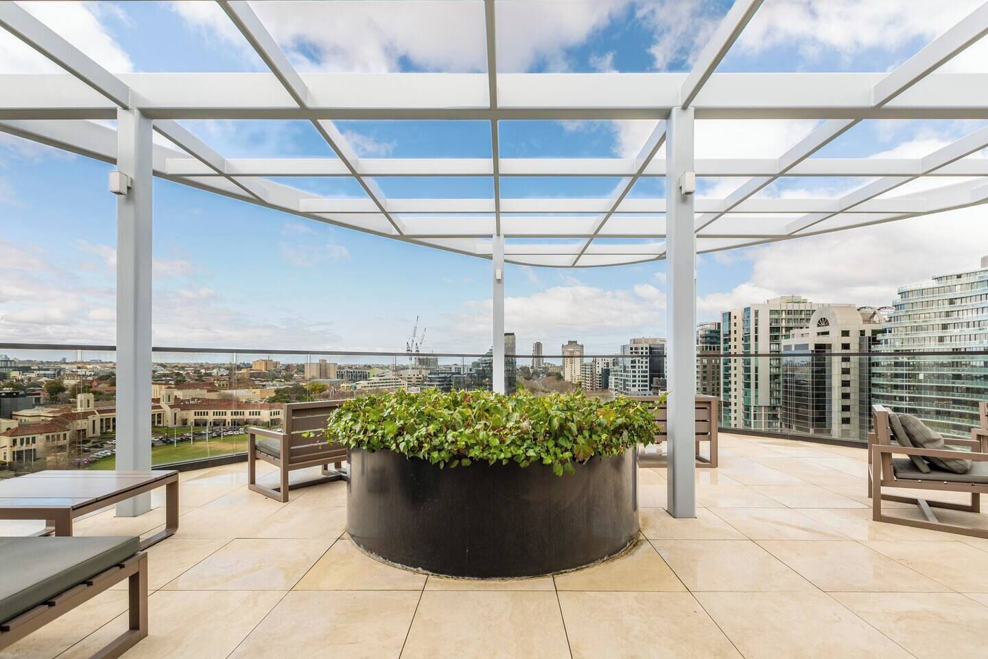 A rooftop terrace with a pergola, seating, and a large planter with greenery.