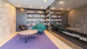 A modern library with bookshelves, a teal armchair, and a small table. - Parque Canopy Lakeside Living with Infinity Pool (Melbourne)