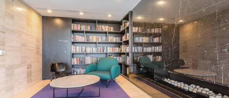 A modern library with bookshelves, a teal armchair, and a small table.