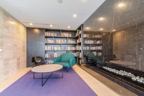 A modern library with bookshelves, a teal armchair, and a small table. - Parque Canopy Lakeside Living with Infinity Pool (Melbourne)