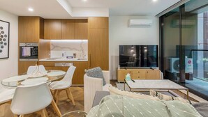 A modern living room with a dining area, a kitchen, a flat-screen TV, and a large window. - Parque Canopy Lakeside Living with Infinity Pool (Melbourne)