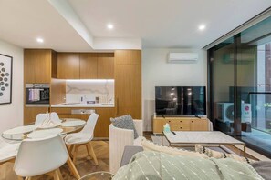 A modern living room with a dining area, a kitchen, a flat-screen TV, and a large window. - Parque Canopy Lakeside Living with Infinity Pool (Melbourne)