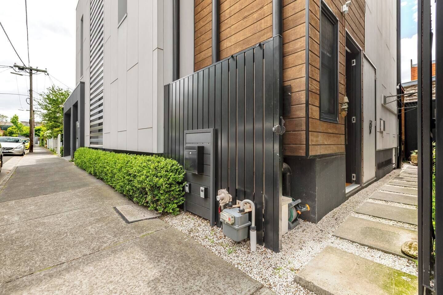 A modern building with a grey facade, a wooden panel section, and a black metal gate.