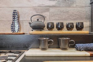 A kitchen with a gas stove, a kettle, and a set of four dark-colored cups on a wooden shelf. - Hikari Haven Richmonds Creative Spirit near Cafs (Richmond)