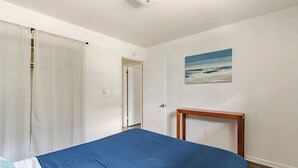 A bedroom with a bed, a painting, and a wooden bedside table. - Budget-Friendly 2BR/2BA • Walkable to Events (Virginia Beach)
