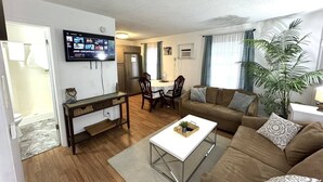 A living room with a sofa, coffee table, TV, and a dining area with chairs and a table. - Budget-Friendly 2BR/2BA • Walkable to Events (Virginia Beach)