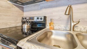 Une cuisine équipée d’une cuisinière, d’une bouilloire, d’un évier et d’un distributeur de savon.