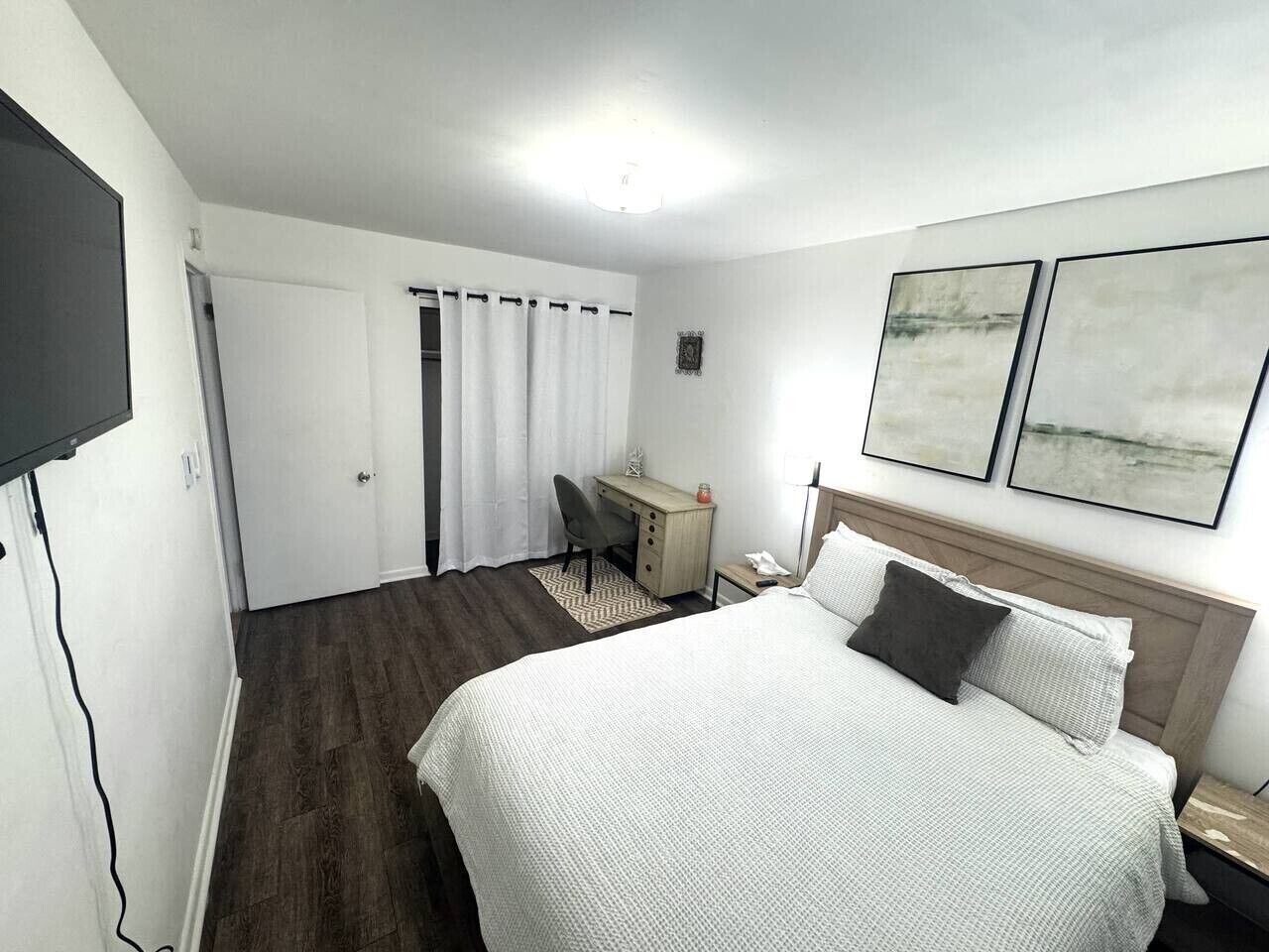 A hotel room with a bed, desk, chair, and artwork on the wall.