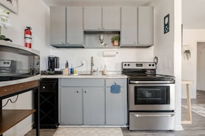 A compact kitchen with grey cabinets, a stainless steel oven, and a coffee machine. - ViBe District 2BR/2BA On 19th Street (Virginia Beach)