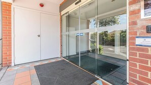 Entrada d'un edifici amb una porta de vidre, un detector de fum i un senyal que indica la comunitat de propietaris.