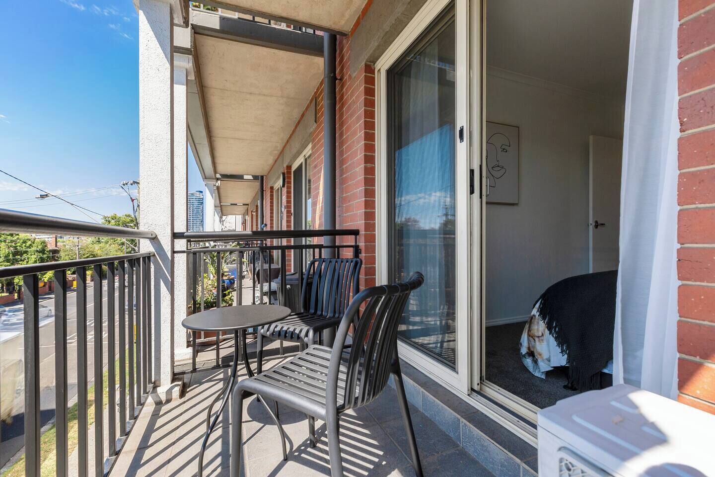 Ein Balkon mit Tisch und Stühlen, eine Schiebetür aus Glas und Blick auf die Straße.