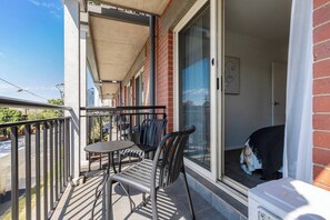 Ein Balkon mit Tisch und Stühlen, eine Schiebetür aus Glas und Blick auf die Straße.