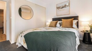 Habitació d'hotel amb un llit, un mirall rodó, un quadre i una taula auxiliar amb una làmpada.