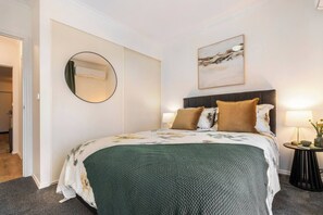 Ein Hotelzimmer mit einem Bett, einem runden Spiegel, einem Gemälde und einem Nachttisch mit einer Lampe.