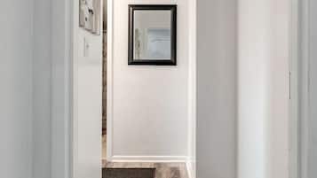 A hallway with a wooden floor, a rug, a framed picture on the wall, and a decorative wall piece.