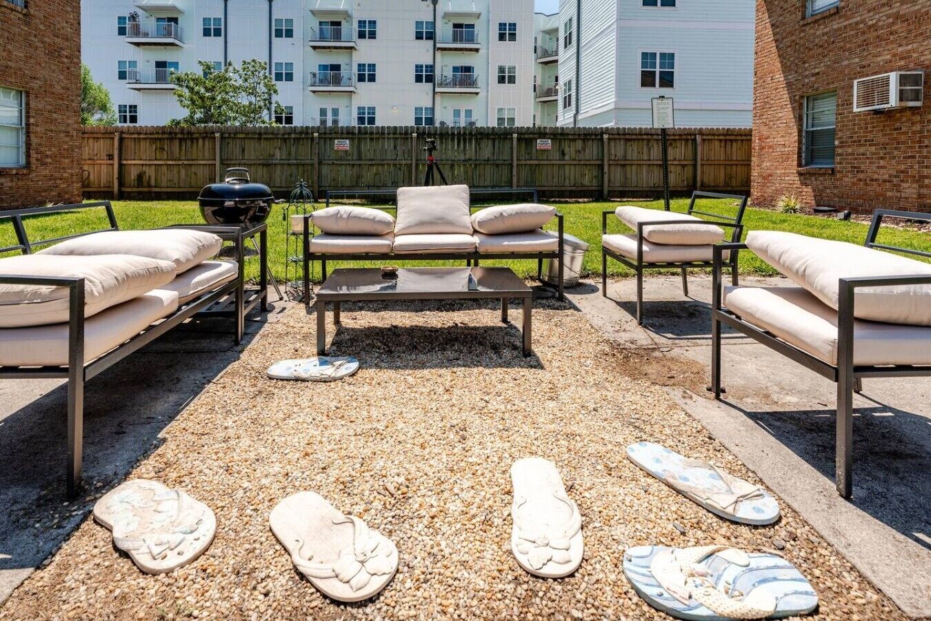 An outdoor seating area with a central table and sofas, surrounded by a gravel surface with footprints.