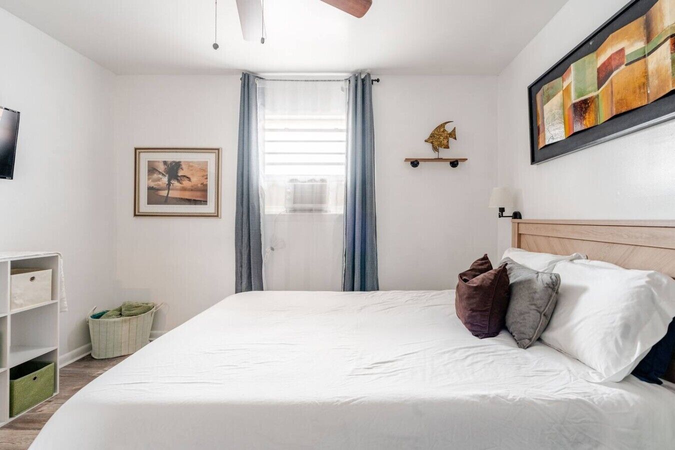 A neatly arranged bedroom with a bed, a framed picture, a shelf with a decorative item, and a window with curtains.