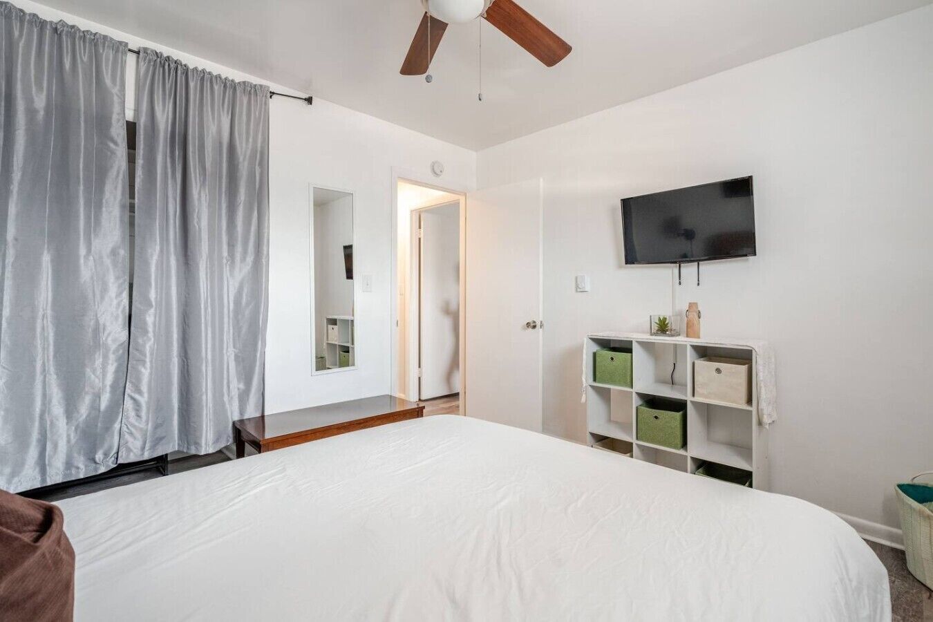 Ein Schlafzimmer mit einem großen Bett, einem Deckenventilator, einem an der Wand montierten Fernseher und einem Kleiderschrank mit Aufbewahrungsboxen.